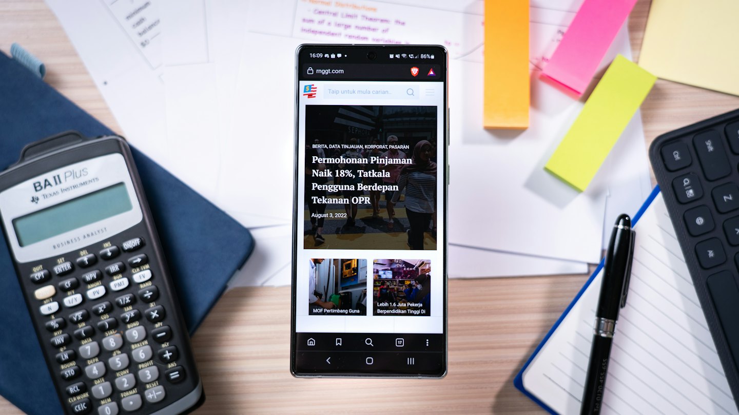 Smartphone showing business news on a wooden desk with office supplies.
