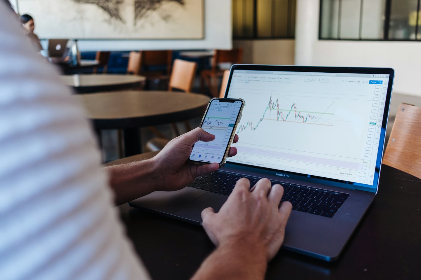 Hands analyzing financial charts on laptop and smartphone.